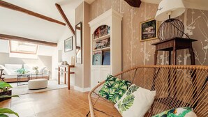 A cozy living room with a rattan sofa, wooden flooring, and a bookshelf.