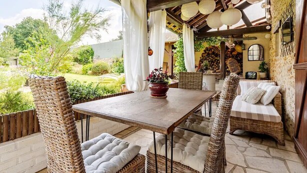 A covered patio with wicker furniture, a table, and a cushioned bench.