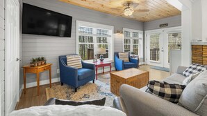 A living room with a wooden ceiling, a television mounted on the wall, and a large window with blinds. - Alpine Bear Trail - Comfortable Townhome in the Innsbruck Golf Community (Helen)