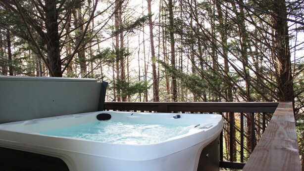 A hot tub on a wooden deck surrounded by tall trees. - Alpine Bear Trail - Comfortable Townhome in the Innsbruck Golf Community (Helen)