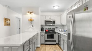 A modern kitchen with white cabinets, stainless steel appliances, and a wooden floor. - Alpine Bear Trail - Comfortable Townhome in the Innsbruck Golf Community (Helen)