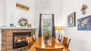 A dining room with a stone fireplace, wooden dining table, and chairs. There are wall decorations including a 'FAMILY LOVE' sign, a world map, and a clock. - Alpine Bear Trail - Comfortable Townhome in the Innsbruck Golf Community (Helen)