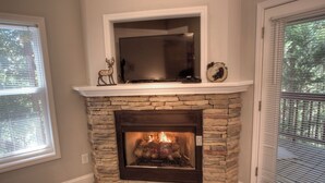 A stone fireplace with a television above it, flanked by windows with blinds. - Lark’s Nest Mtn View - See Yonah Mountain from the Front Porch! (Helen)