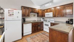 A kitchen with wooden cabinets, white appliances, granite countertops, and a patterned rug. - Lark’s Nest Mtn View - See Yonah Mountain from the Front Porch! (Helen)