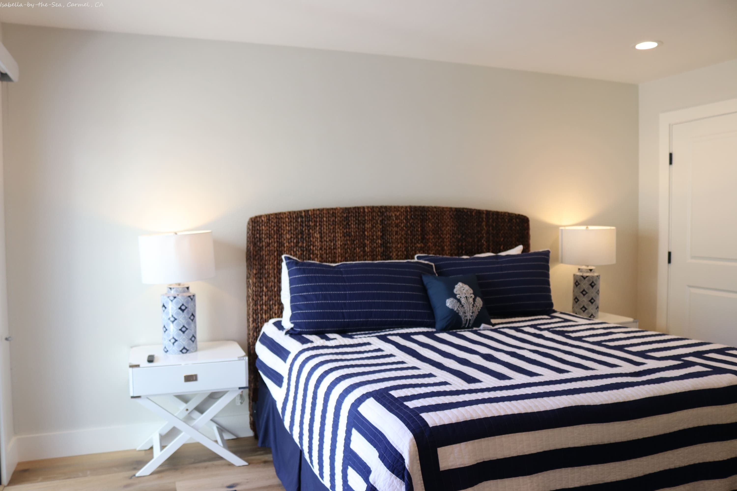 A bedroom with a striped bedspread, two bedside lamps, a white nightstand, and a patterned headboard.