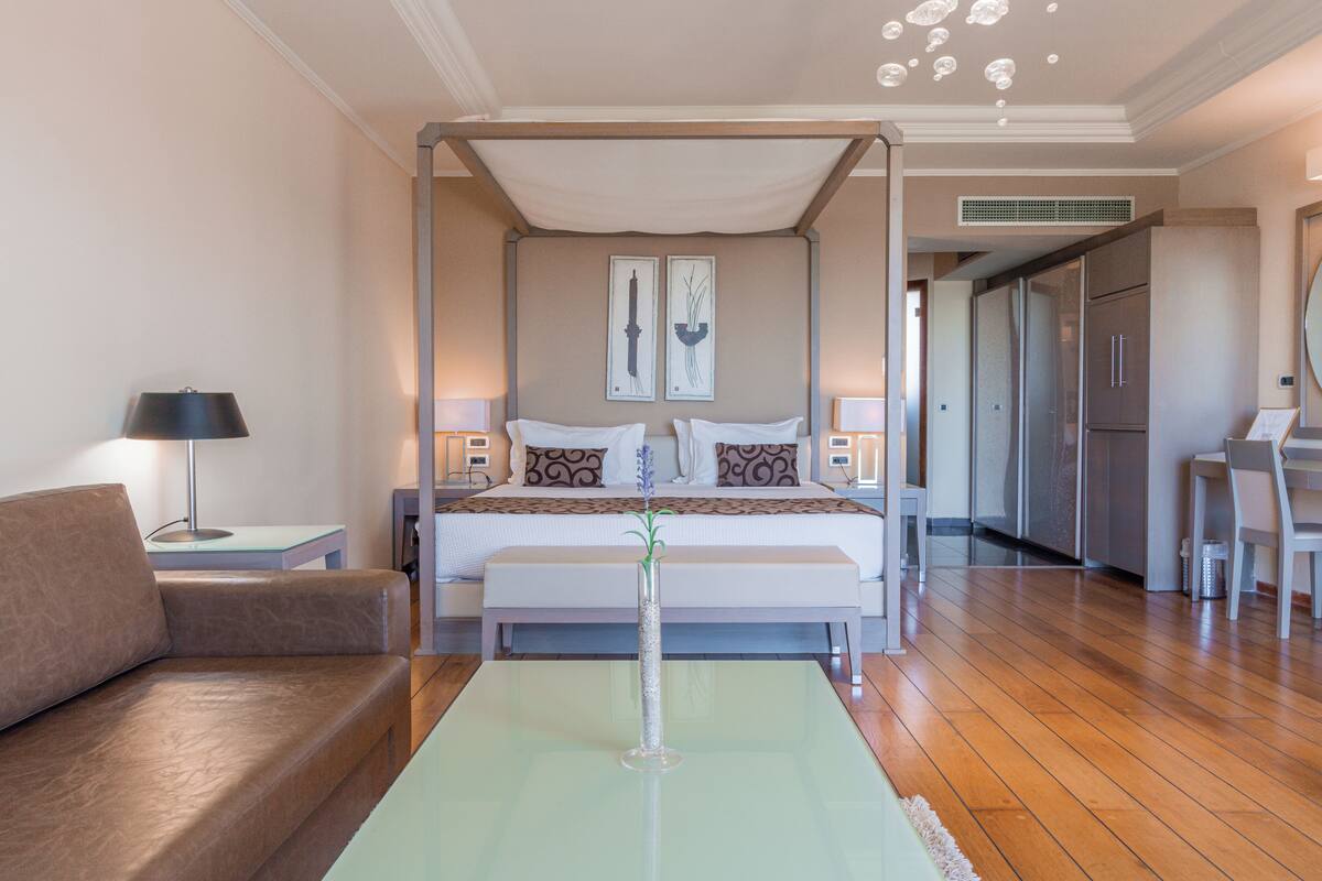A bedroom with a four-poster bed, bedside tables, a nightstand, a sofa, and a dining area with a chair.