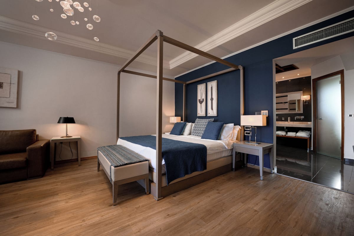 A modern bedroom with a four-poster bed, a bedside table, a nightstand, a bench, and a mirror.