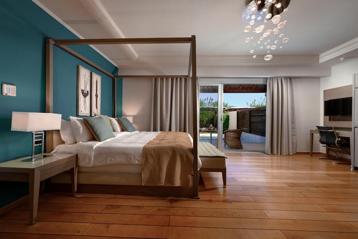 A modern bedroom with a four-poster bed, a bedside table with a lamp, and a view of the outdoor patio.