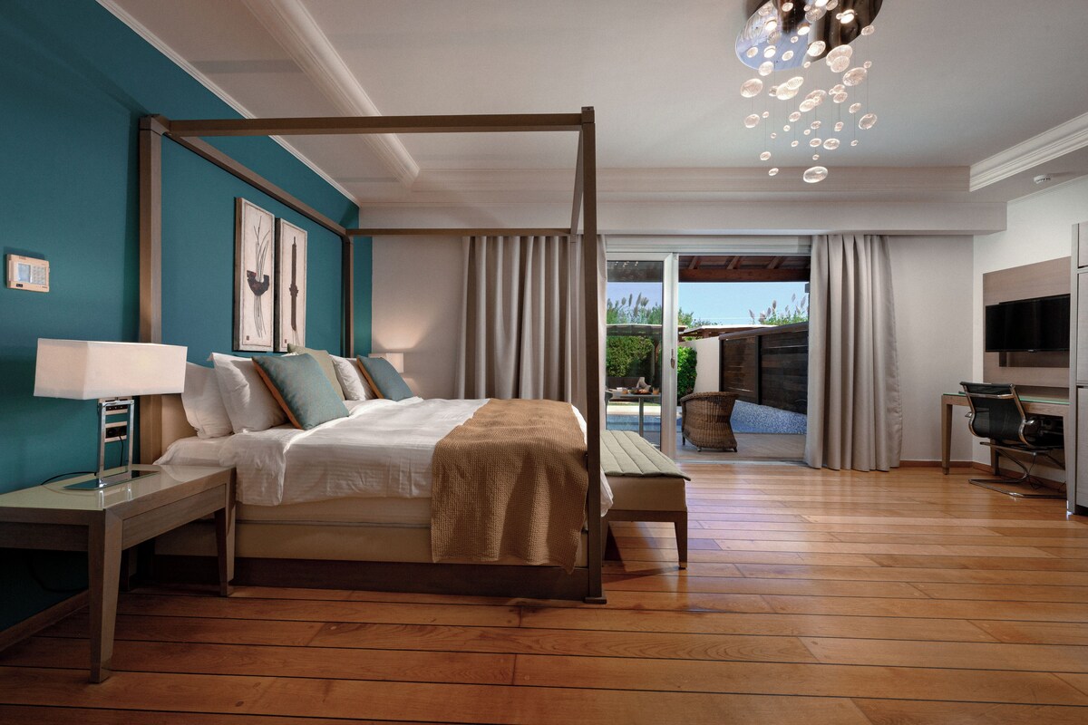 A bedroom with a four-poster bed, a desk, a chair, a TV, and a view of the outdoors.