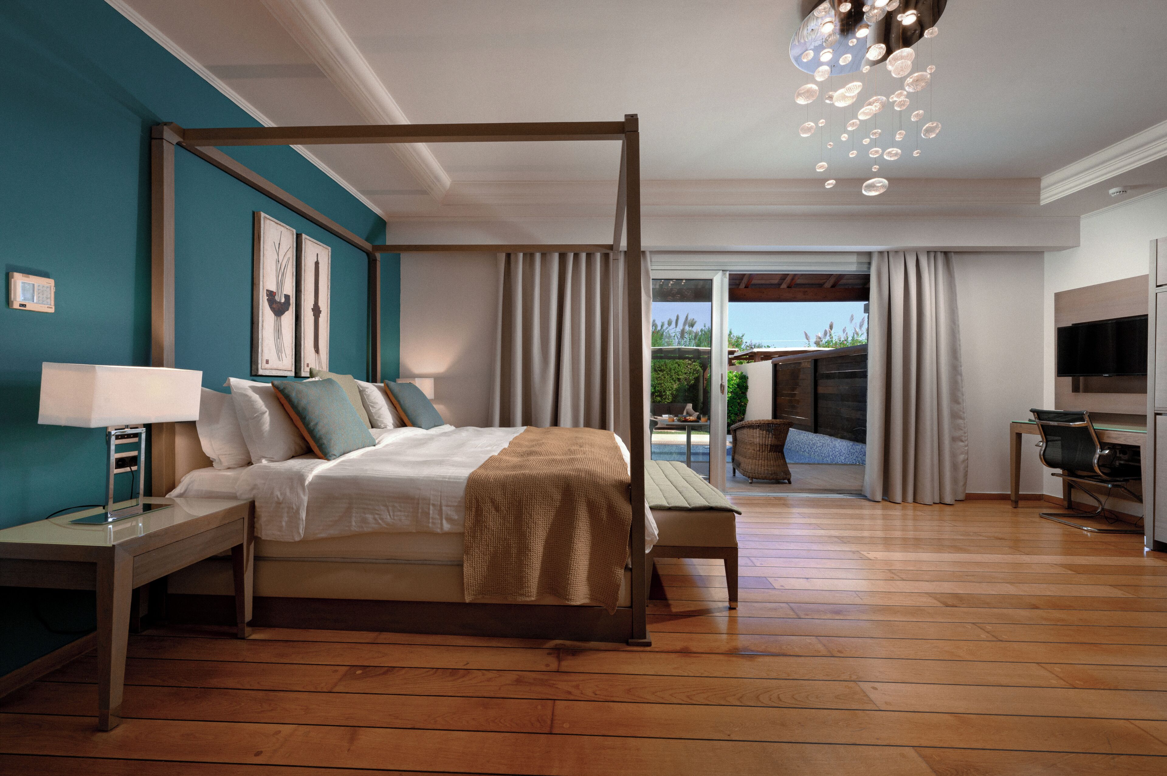 A bedroom with a four-poster bed, a desk, a chair, a TV, and a view of the outdoors.