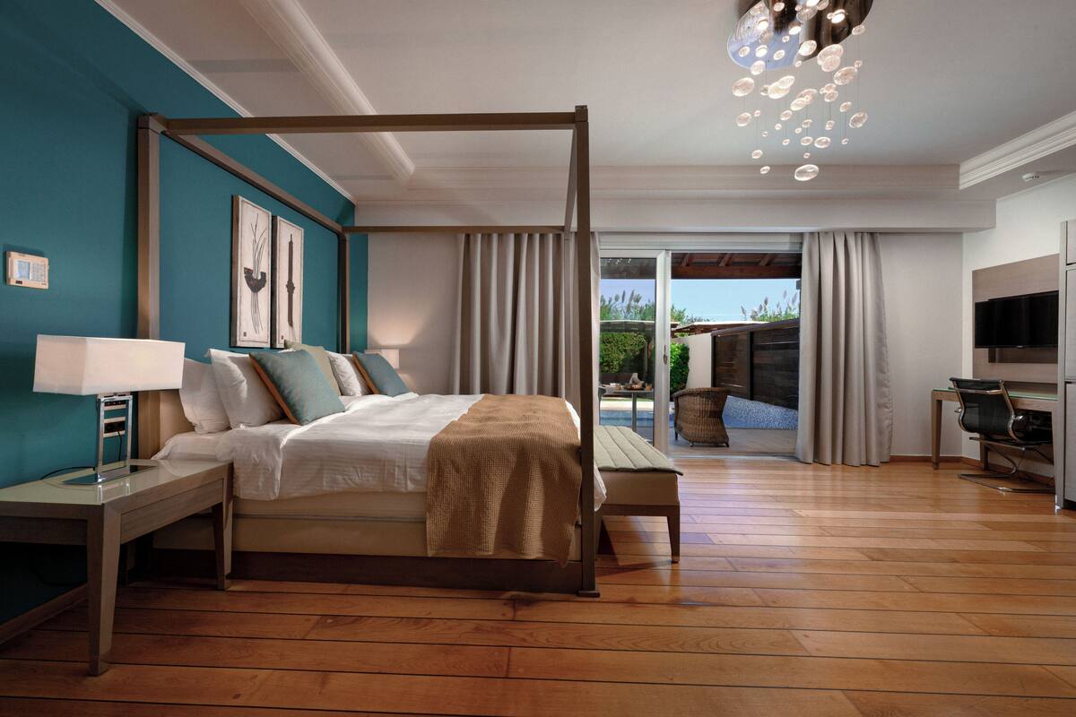 A bedroom with a four-poster bed, a desk, a chair, a TV, and a view of the outdoors.