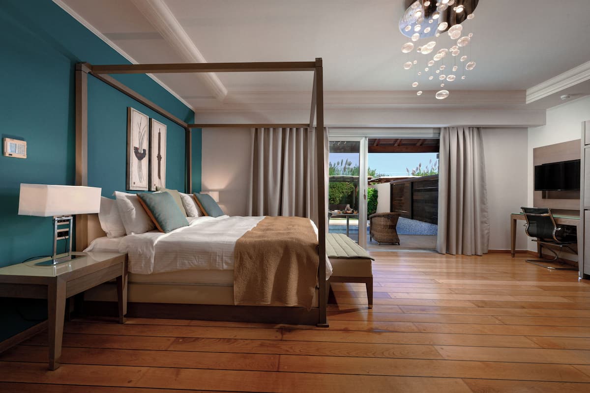 A bedroom with a four-poster bed, a desk, a chair, a TV, and a view of the outdoors.