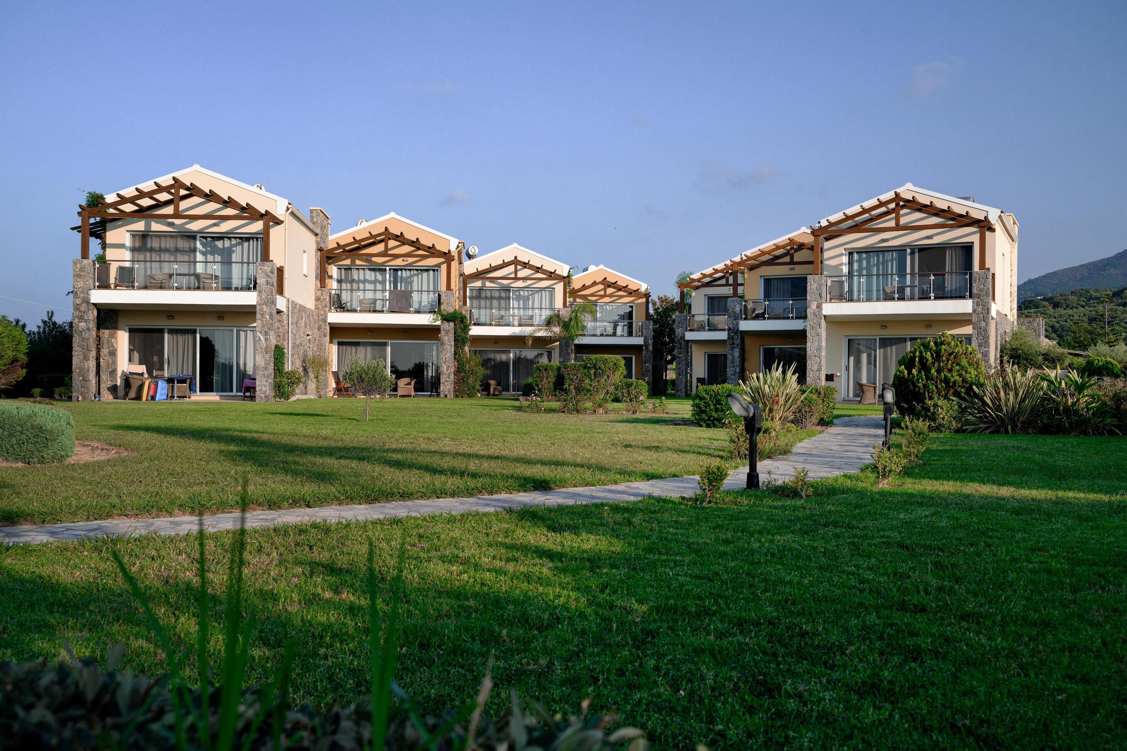 A modern multi-story hotel with a well-maintained lawn, outdoor seating, and a clear view of the surrounding landscape.