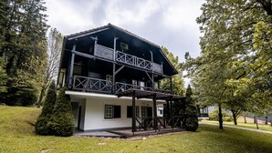 A two-story wooden building with a balcony, surrounded by trees and grass. - Apartments Amy (Podcetrtek)