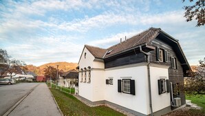 A two-story house with a white exterior and dark roof, a driveway, and a grassy yard. - Apartments Amy (Podcetrtek)