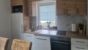 A modern kitchen with wooden cabinets, a built-in microwave, a sink, and a window with blinds. - Apartments Amy (Podcetrtek)