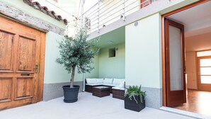 A courtyard with a wooden door, a potted tree, a white sofa, and a small planter. - Apartments Amavi (Izola)