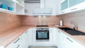 A modern kitchen with white cabinets, a black countertop, a stainless steel oven, and a black sink. - Apartments Amavi (Izola)