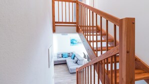 A staircase with wooden railings leading to a living area with a light-colored sofa and a blue pillow. - Apartments Amavi (Izola)