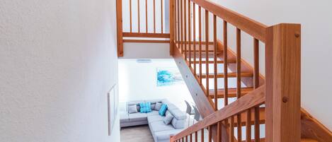 A staircase with wooden railings leading to a living area with a light-colored sofa and a blue pillow.
