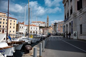 A marina with boats docked along a waterfront, buildings with classical architecture, and a clock tower in the background. - Apartments Amavi (Izola)