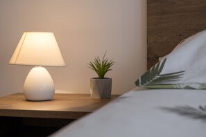 Una mesita de noche con una lámpara blanca y una pequeña planta en maceta.