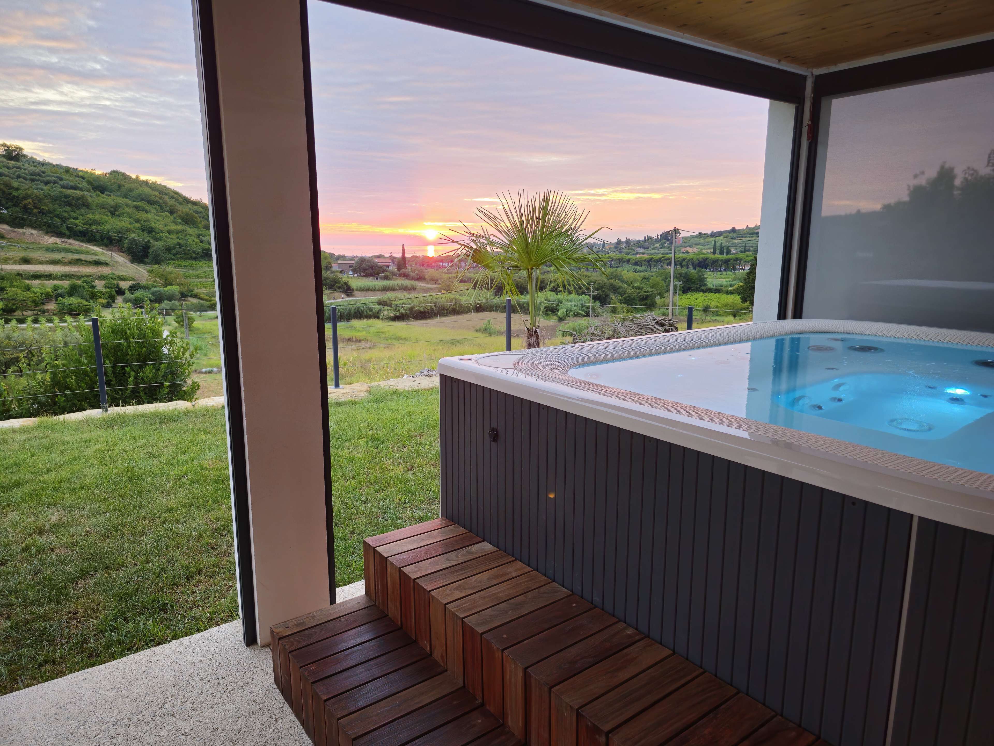 A hot tub with a wooden deck and a view of a sunset over a hilly landscape.