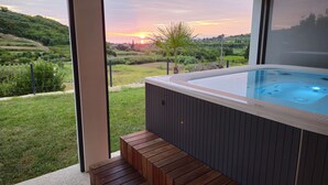 Uma banheira de hidromassagem com um deck de madeira e vista para um pôr do sol sobre uma paisagem montanhosa.