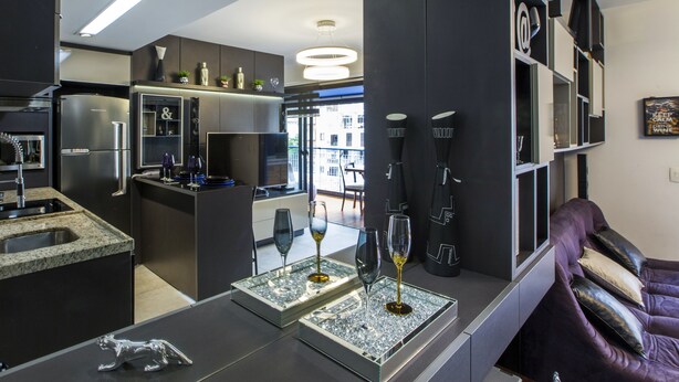 Una cocina moderna con una isla integrada, electrodomésticos de acero inoxidable y una zona de estar con un sofá y cojines morados.