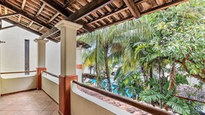 A covered balcony with a view of a tropical garden and a pool. - Colorful & Private 2-Bedroom Condo Just a Short Walk from the Beach (Coco)
