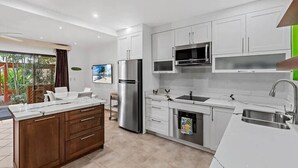 A modern kitchen with white cabinets, stainless steel appliances, and a large island with a sink. - Colorful & Private 2-Bedroom Condo Just a Short Walk from the Beach (Coco)
