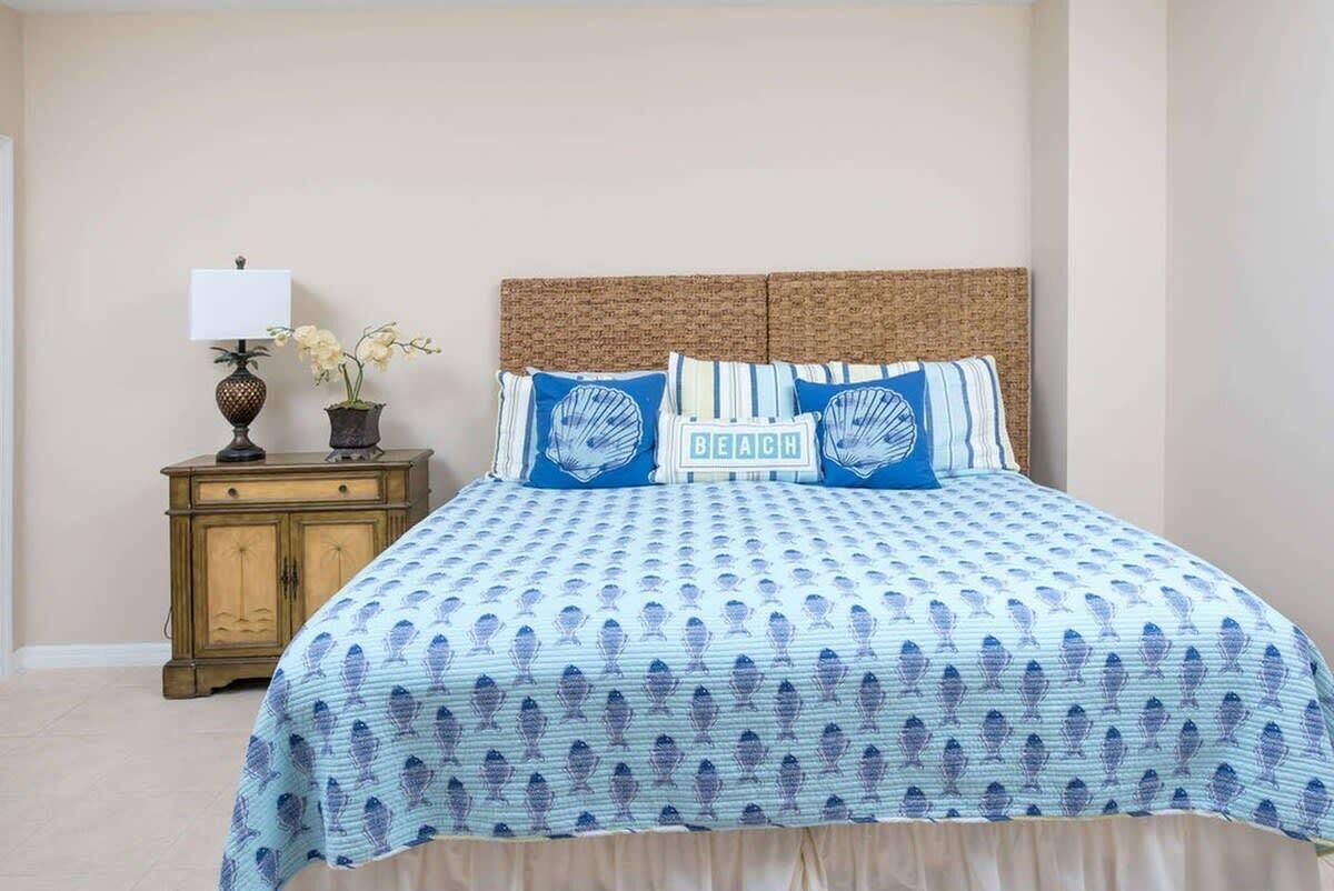 A bedroom with a bed, a nightstand, a lamp, and a potted plant.