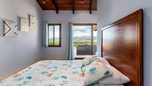 A bedroom with a large bed, wooden headboard, and a view of the outdoors through a sliding glass door. - Chic Cliffside Condo w/ Two Balconies Offering Spectacular Ocean & Mountain Views (Playa Flamingo)