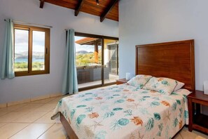 Een slaapkamer met een groot bed, een houten hoofdeinde en uitzicht op een balkon met een mooi landschap.