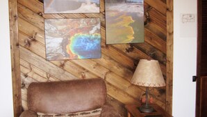 A brown leather armchair with a bear-themed pillow, a wooden side table with a lamp, and three framed pictures on a wooden wall. - Morning Glory-comfortable Yellowstone retreat; just minutes from YNP West Gate (West Yellowstone)