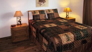 A bedroom with a large bed, two bedside tables, a nightstand, a wall-mounted lamp, and a painting of a moose. - Morning Glory-comfortable Yellowstone retreat; just minutes from YNP West Gate (West Yellowstone)