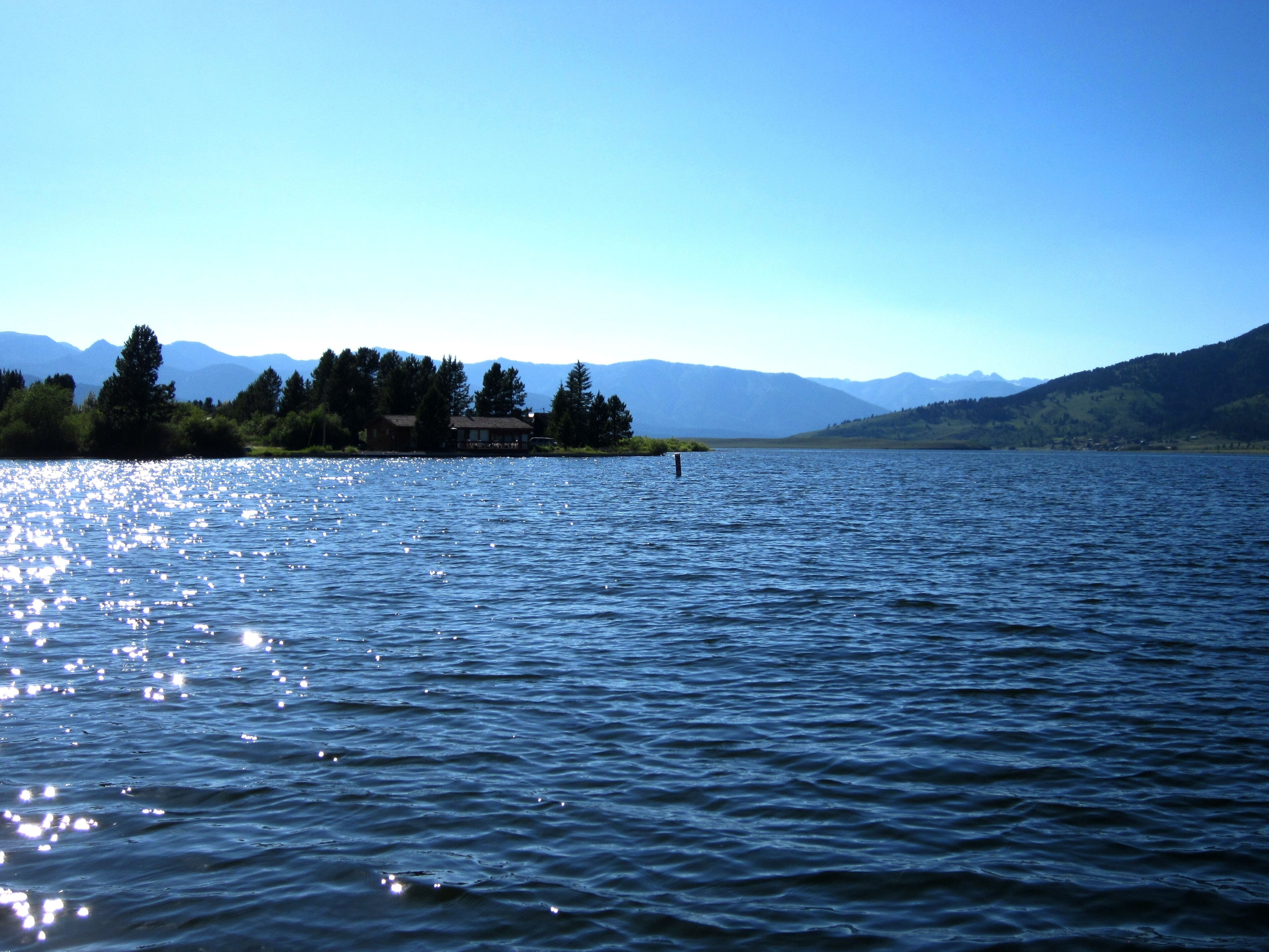 A calm lake with a house on the shore, surrounded by mountains.