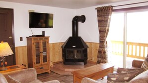 A living room with a fireplace, a television mounted on the wall, and a wooden cabinet. - Morning Glory-comfortable Yellowstone retreat; just minutes from YNP West Gate (West Yellowstone)