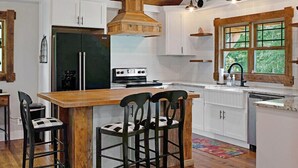 A kitchen with white cabinets, a wooden island with chairs, a stove, and a refrigerator. - Farmhouse just minutes from Hanging Rock, sister property next door ID#3934130 (King)