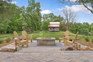 Une terrasse extérieure avec des fauteuils Adirondack, un foyer et une vue sur un chalet rustique au loin.