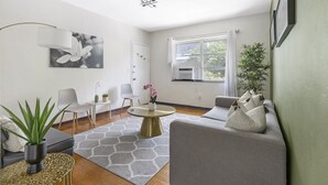 Ett modernt vardagsrum med en grå soffa, ett runt soffbord och ett stort fönster med gardiner.