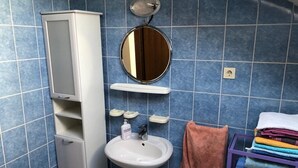 Une salle de bain avec un meuble blanc, un lavabo, un miroir et un porte-serviettes sur lequel sont pliées des serviettes.