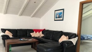 Un salon avec un canapé d’angle en cuir noir, une table basse en bois et un tableau encadré au mur.
