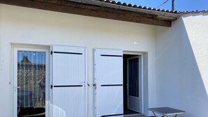 A building with two white doors, a small patio with a table and chairs, and a stone-tiled entrance. - Furnished duplex studio with air-conditioned parking space (Surgères)