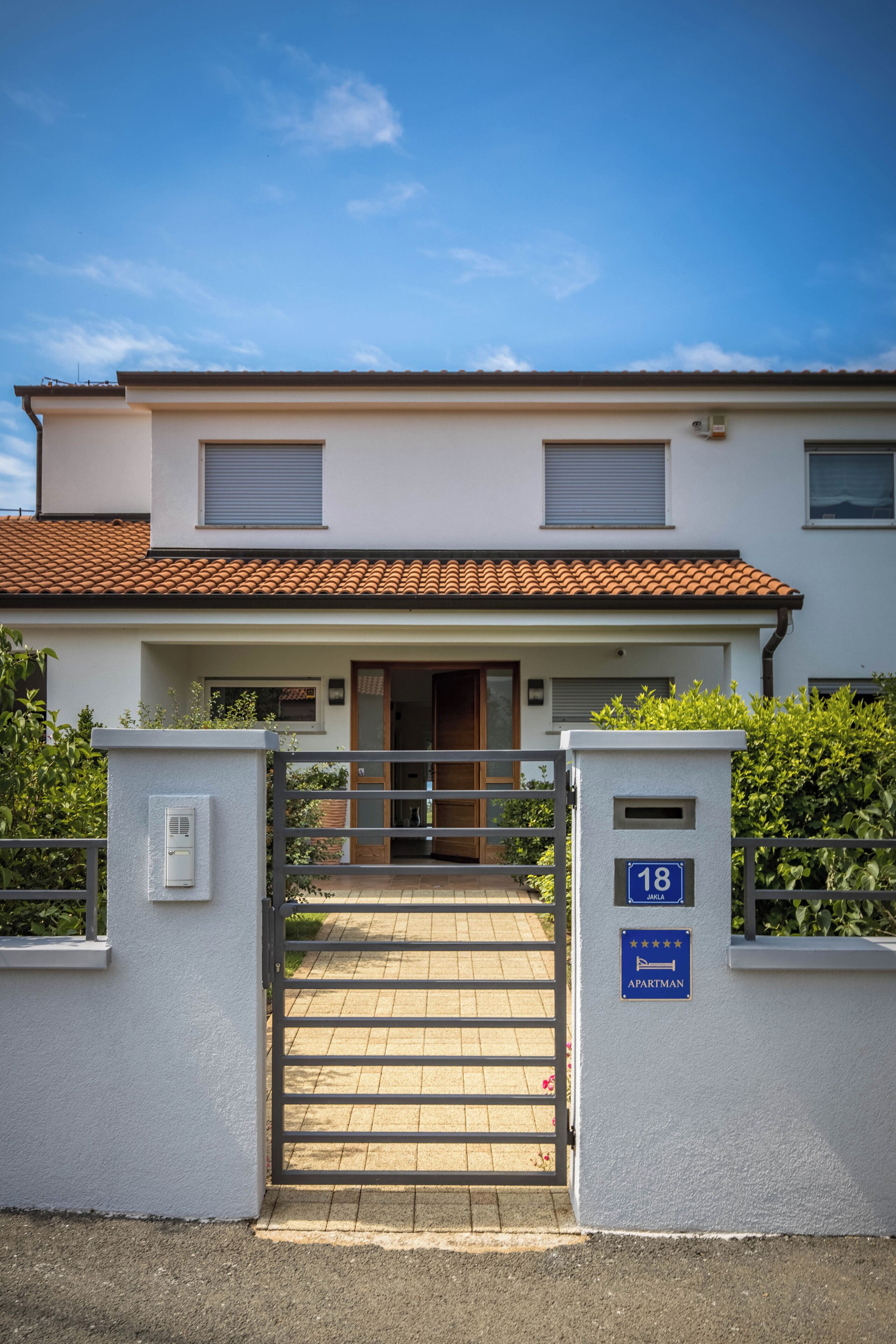 Un immeuble à deux étages, doté d’un toit en tuiles, d’une entrée fermée par un portail et d’une enseigne indiquant qu’il s’agit d’un immeuble d’appartements.