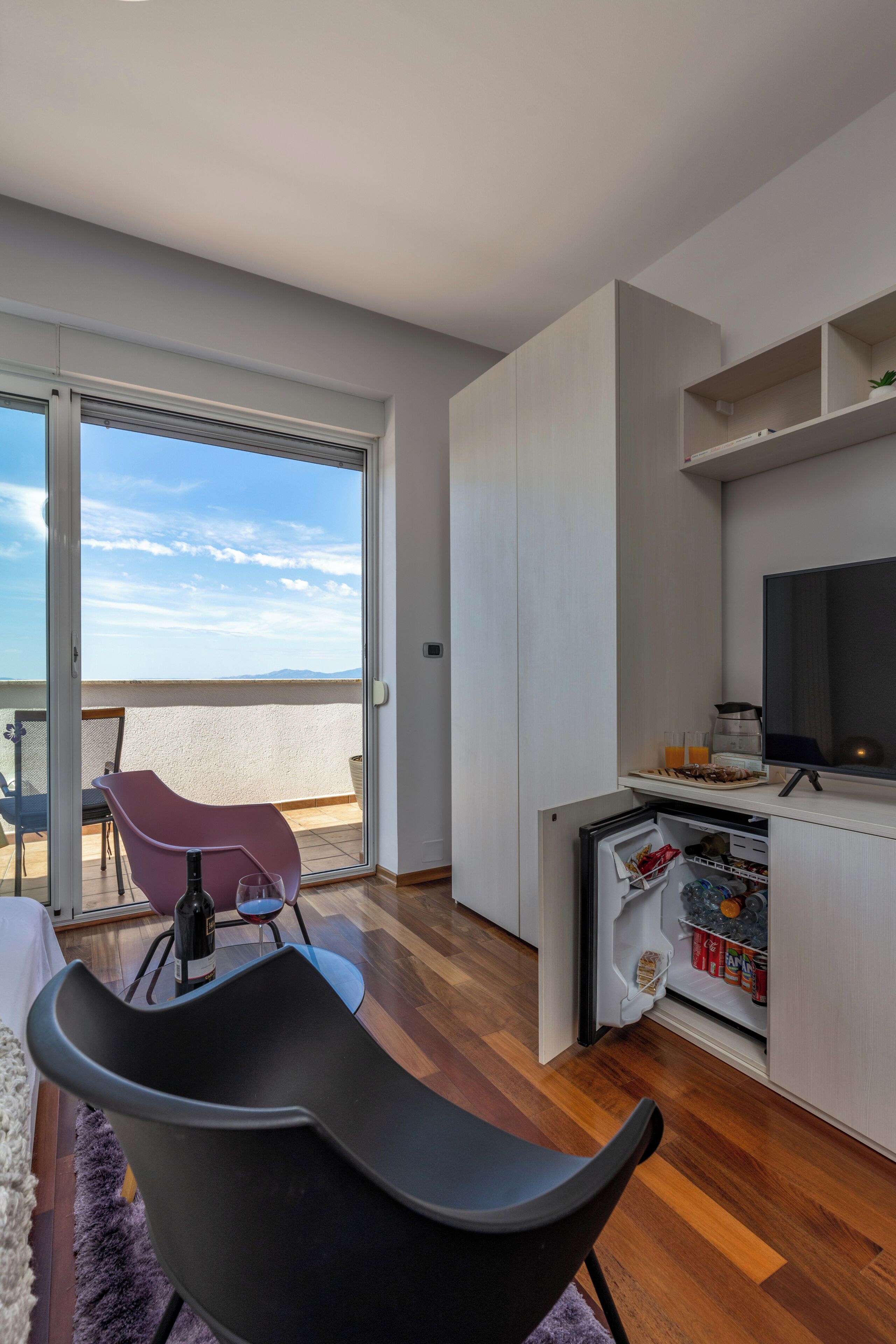 Un apartamento moderno con balcón, comedor, cocina con televisor y un refrigerador pequeño.