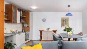 A modern kitchen with wooden cabinets, a dining area with a table and chairs, and a living room with a sofa. - Terra Magica Deluxe Apartment OR Room with Private Parking, Terrace and Sea View (Cavle)