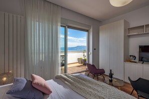 A modern bedroom with a large bed, a view of the balcony, and a small kitchenette. - Terra Magica Deluxe Apartment OR Room with Private Parking, Terrace and Sea View (Cavle)