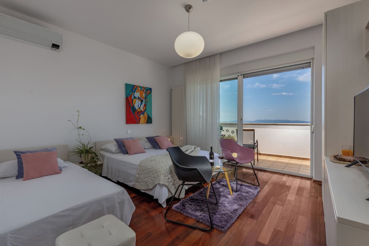 A modern hotel room with two beds, a dining area, and a balcony with a view.