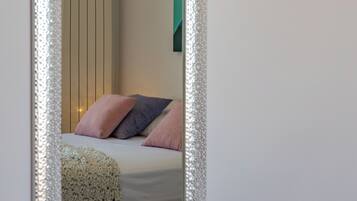 Un dormitorio con cama, almohadas, mesita de noche y espejo.